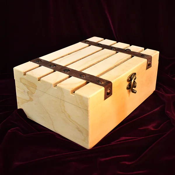 Caja de madera artesanal tipo baúl con tapa de tablones ranurados, herrajes de metal dorado y correas de cuero oscuro con remaches, sobre un fondo de tela de terciopelo granate